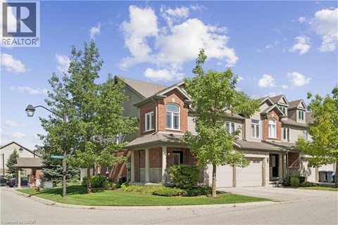 A house with a brown roof and a white garage door is surrounded by trees and other houses.
