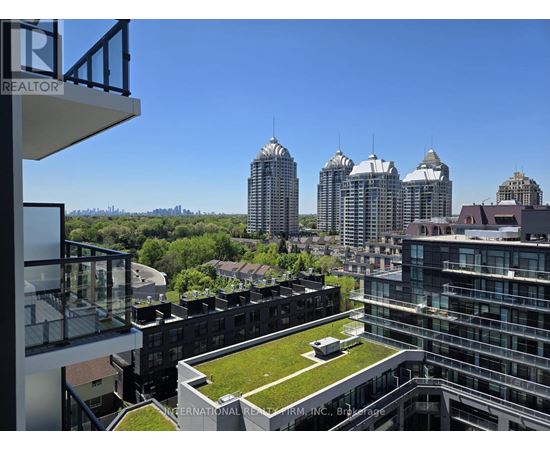 A view from a balcony of a building with a green lawn and several tall buildings in the background.