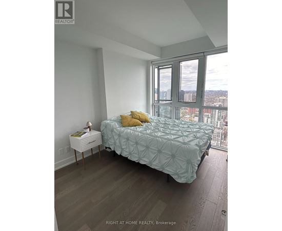 A bedroom with a bed, nightstand, and a window overlooking a cityscape.