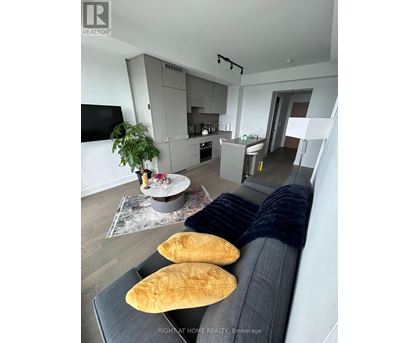 A modern living room with a grey sofa and a grey kitchen in the background.