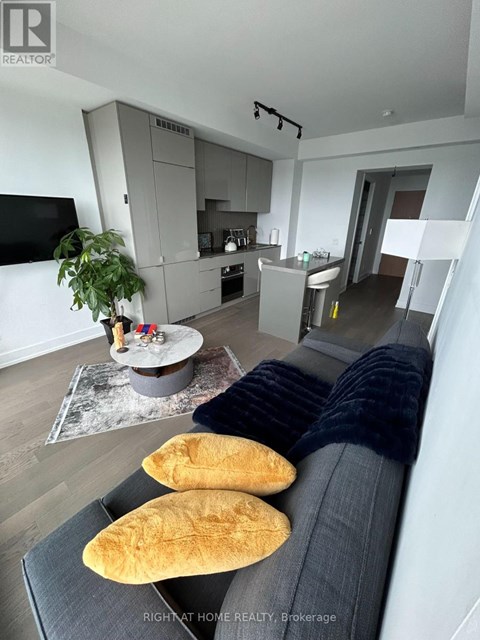 A modern living room with a grey sofa and a grey kitchen in the background.