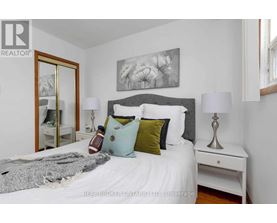 A bedroom with a white bed and a grey headboard with a painting above it.