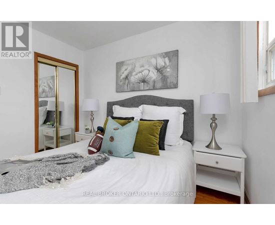 A bedroom with a white bed and a grey headboard with a painting above it.