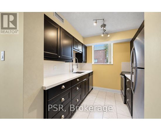 A kitchen with black cabinets and a stainless steel refrigerator.