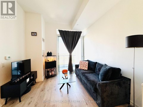 A black couch with a red pillow is in the middle of a living room.