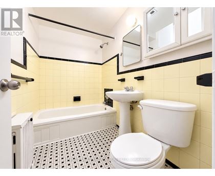 A white toilet sits in a bathroom with yellow tiles.