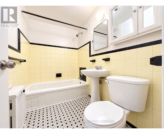 A white toilet sits in a bathroom with yellow tiles.