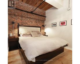 A bedroom with a brick wall and a bed with a white comforter.