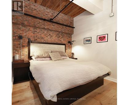 A bedroom with a brick wall and a bed with a white comforter.