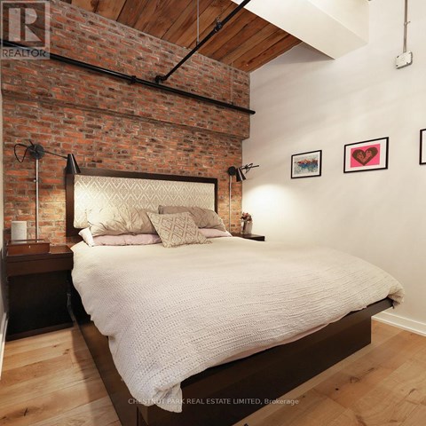 A bedroom with a brick wall and a bed with a white comforter.
