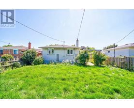 A grassy area with a house in the background and a REALTOR sign in the corner.