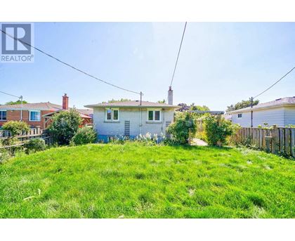 A grassy area with a house in the background and a REALTOR sign in the corner.