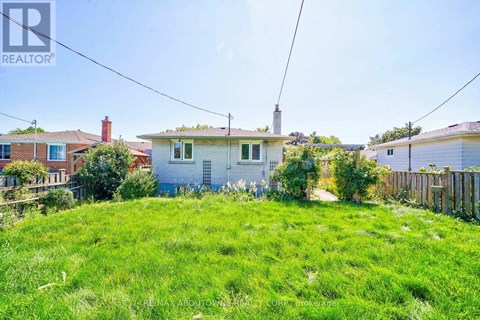 A grassy area with a house in the background and a REALTOR sign in the corner.