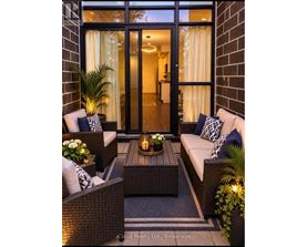 A cozy outdoor seating area with a wicker sofa, chairs, and a table with a lit candle.