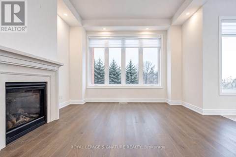 A large, empty room with a fireplace and a view of trees outside the window.