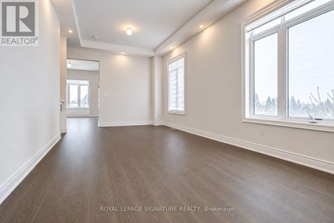 A spacious room with wooden flooring and white walls, with a window showing a snowy landscape outside.