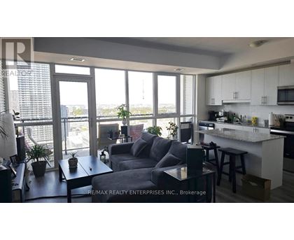 A living room with a grey couch and a kitchen area with white cabinets.