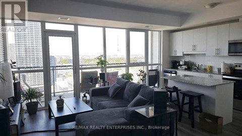 A living room with a grey couch and a kitchen area with white cabinets.
