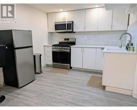 A kitchen with a black fridge, white cabinets, and a marble backsplash.