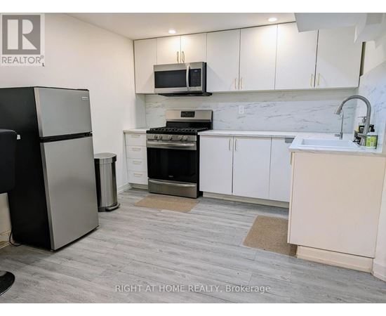 A kitchen with a black fridge, white cabinets, and a marble backsplash.
