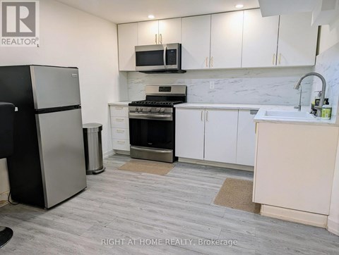 A kitchen with a black fridge, white cabinets, and a marble backsplash.