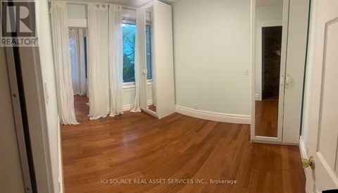 A room with white walls and wooden flooring, with a door on the right side.