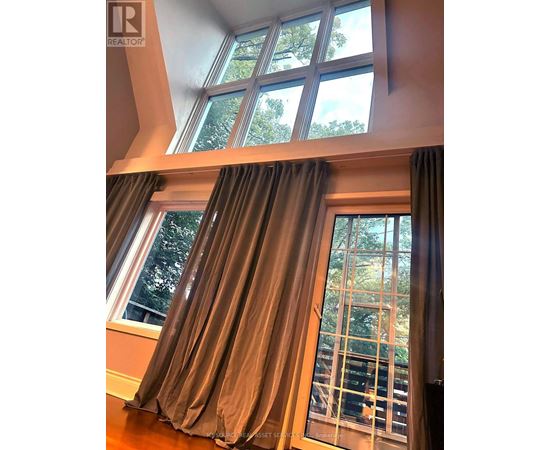 A window with a view of trees and a balcony with a railing.