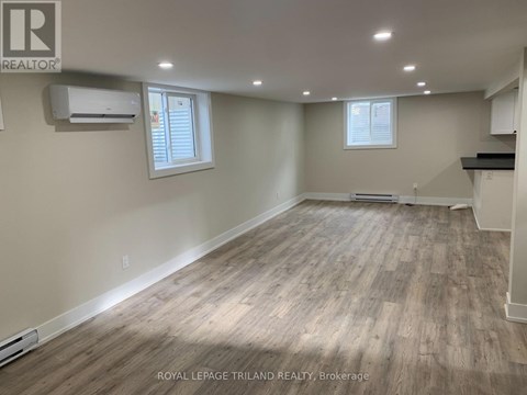 A spacious room with wooden flooring and white walls, with a window and a door visible.