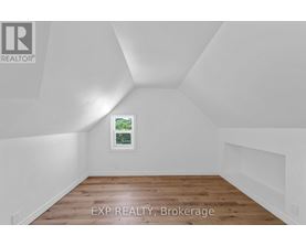 A room with white walls and wooden flooring, with a window showing greenery outside.