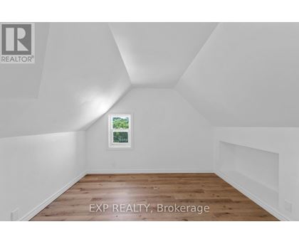 A room with white walls and wooden flooring, with a window showing greenery outside.