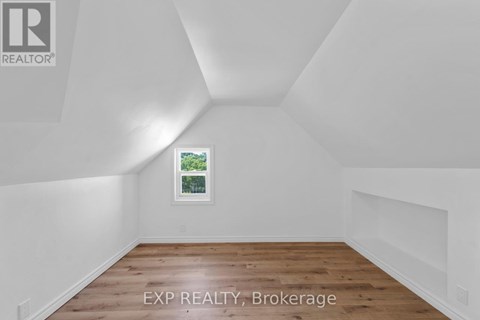 A room with white walls and wooden flooring, with a window showing greenery outside.