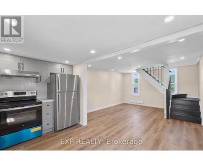A kitchen with a stove top oven, refrigerator, and a staircase.