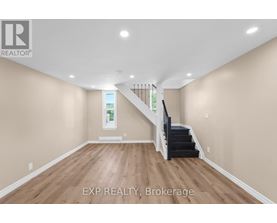 A spacious room with wooden floors and a staircase leading to a second floor.