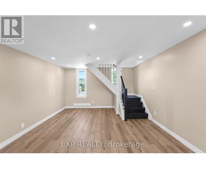 A spacious room with wooden floors and a staircase leading to a second floor.