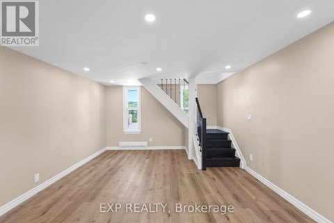 A spacious room with wooden floors and a staircase leading to a second floor.