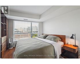 A bedroom with a large bed, a nightstand with a lamp, and a window with blinds.