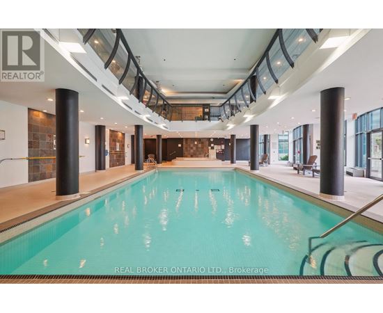 A large indoor swimming pool with a glass ceiling and a Real Broker logo.