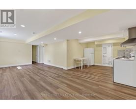 A spacious room with wooden flooring and a white kitchenette.