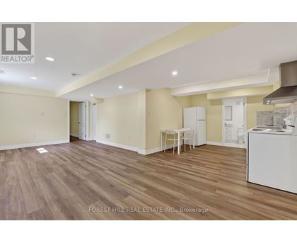 A spacious room with wooden flooring and a white kitchenette.