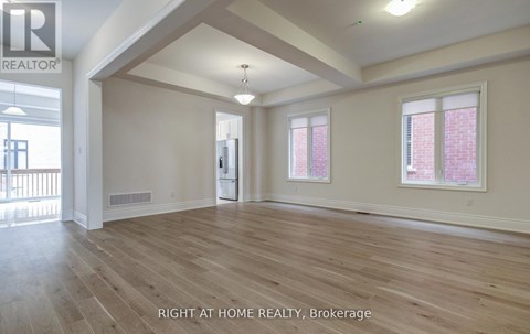 A spacious room with wooden flooring and two windows.