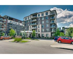 A large, modern apartment building with multiple balconies and a parking lot in front.