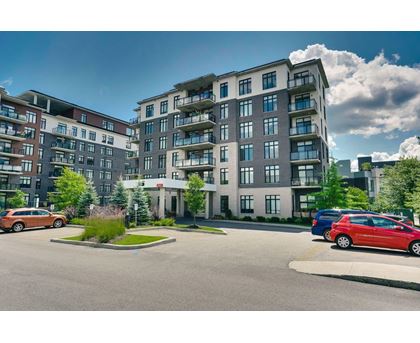 A large, modern apartment building with multiple balconies and a parking lot in front.