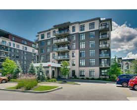 A large, modern apartment building with multiple balconies and a parking lot in front.