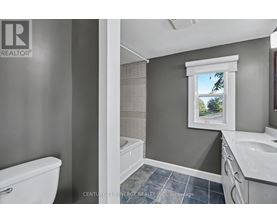 A bathroom with a white toilet, a window with a view of trees, and a sink with a white countertop.