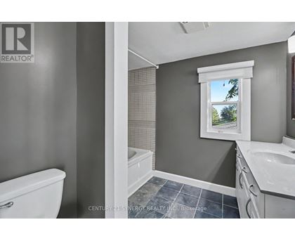 A bathroom with a white toilet, a window with a view of trees, and a sink with a white countertop.