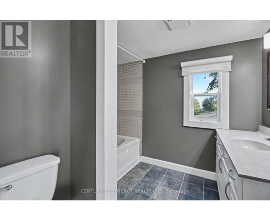 A bathroom with a white toilet, a window with a view of trees, and a sink with a white countertop.