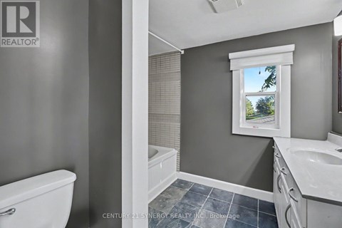 A bathroom with a white toilet, a window with a view of trees, and a sink with a white countertop.