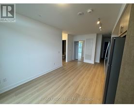 A spacious room with wooden flooring and white walls, with a black refrigerator on the right side.