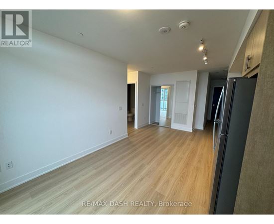 A spacious room with wooden flooring and white walls, with a black refrigerator on the right side.