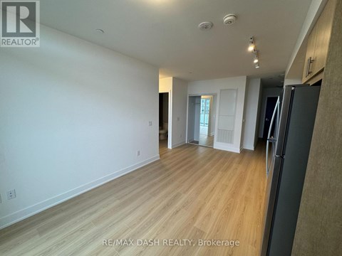 A spacious room with wooden flooring and white walls, with a black refrigerator on the right side.